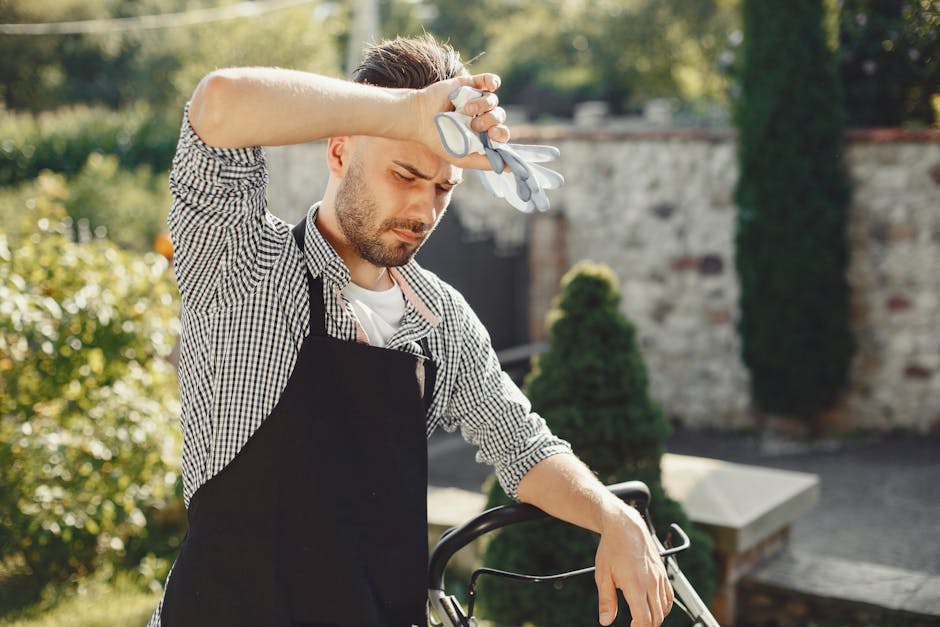 A gardener wearing white gloves is using a small handheld tool to attach a white marker label to a plant or garden feature on a textured, beige fabric surface. To the left, there is a roll of brown tw